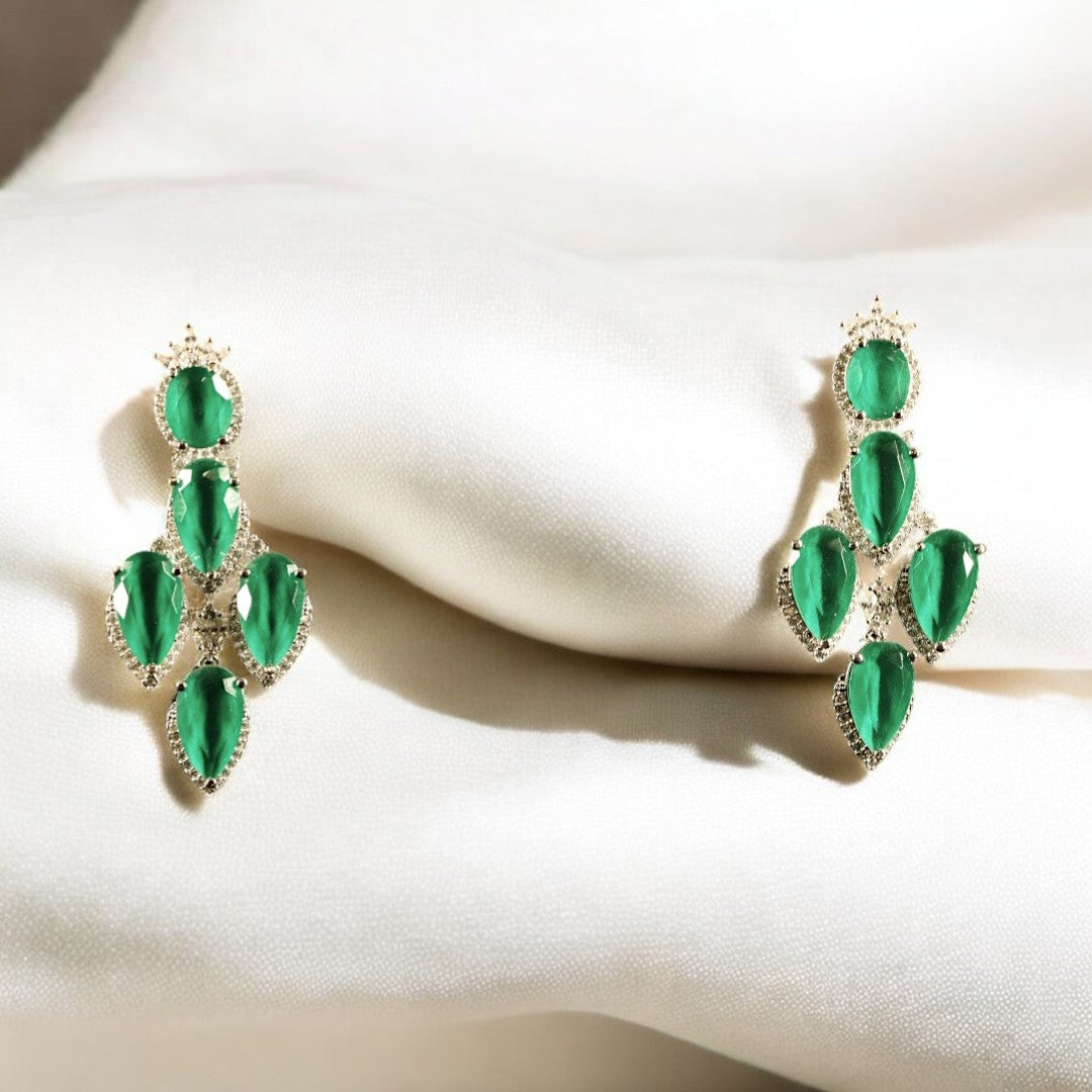 A pair of emerald earrings with a teardrop and marquise cut design, set in a metallic frame