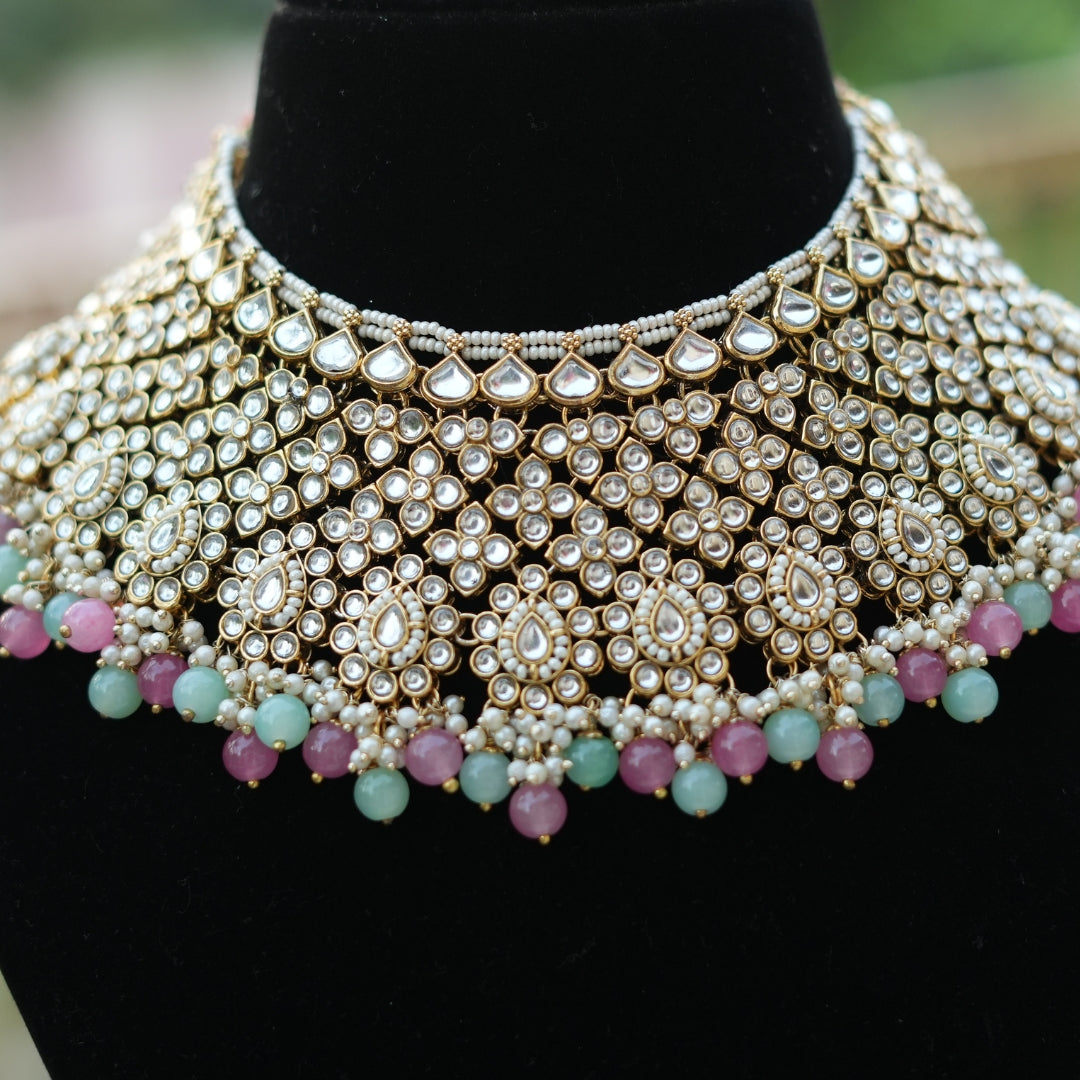 A gold-toned Kundan necklace set with intricate patterns and soft pink and blue stone accents