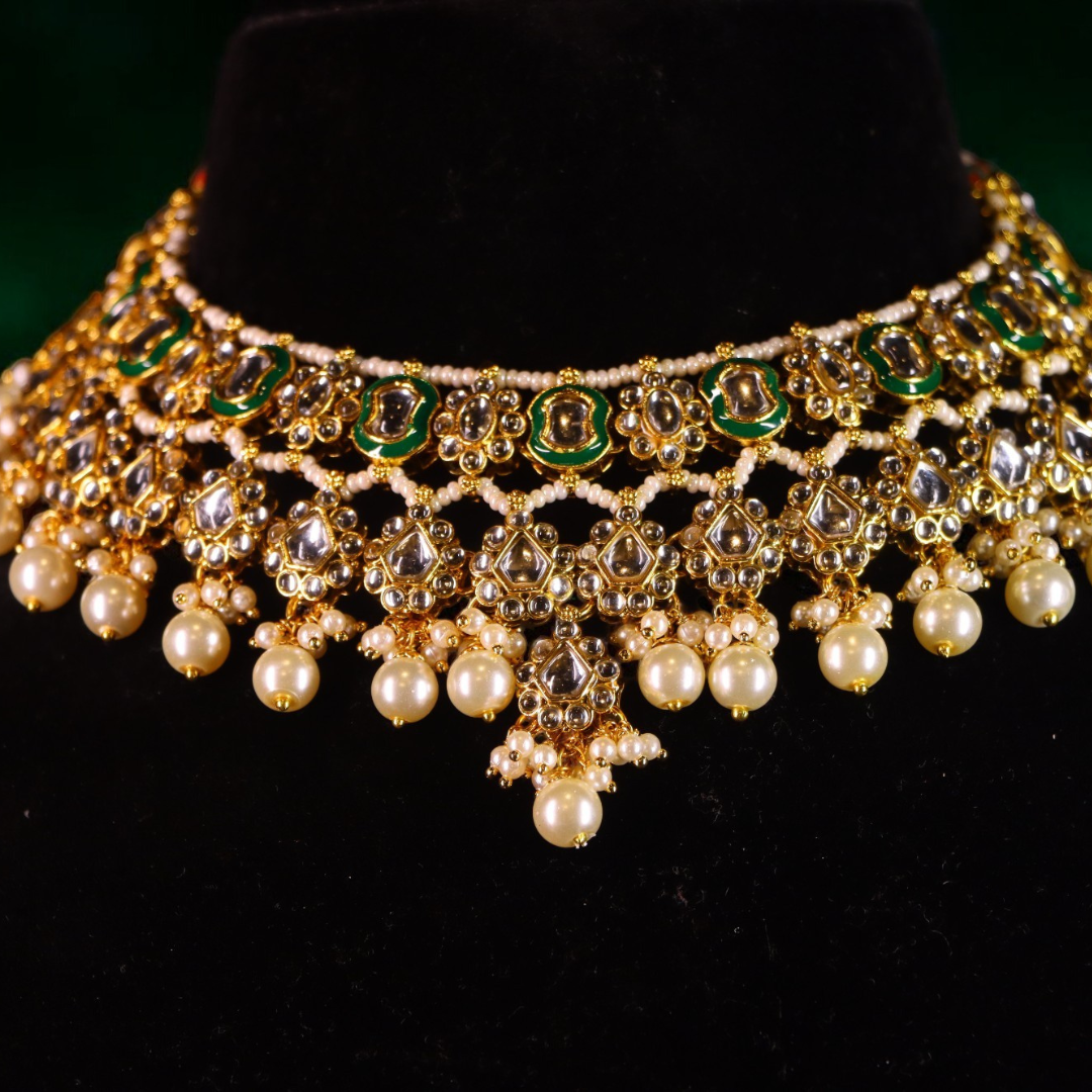 A gold-toned necklace set with green stones and pearl drop detailing