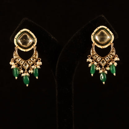 a pair of kundan earrings with green emerald stone accents and intricate craftsmanship
