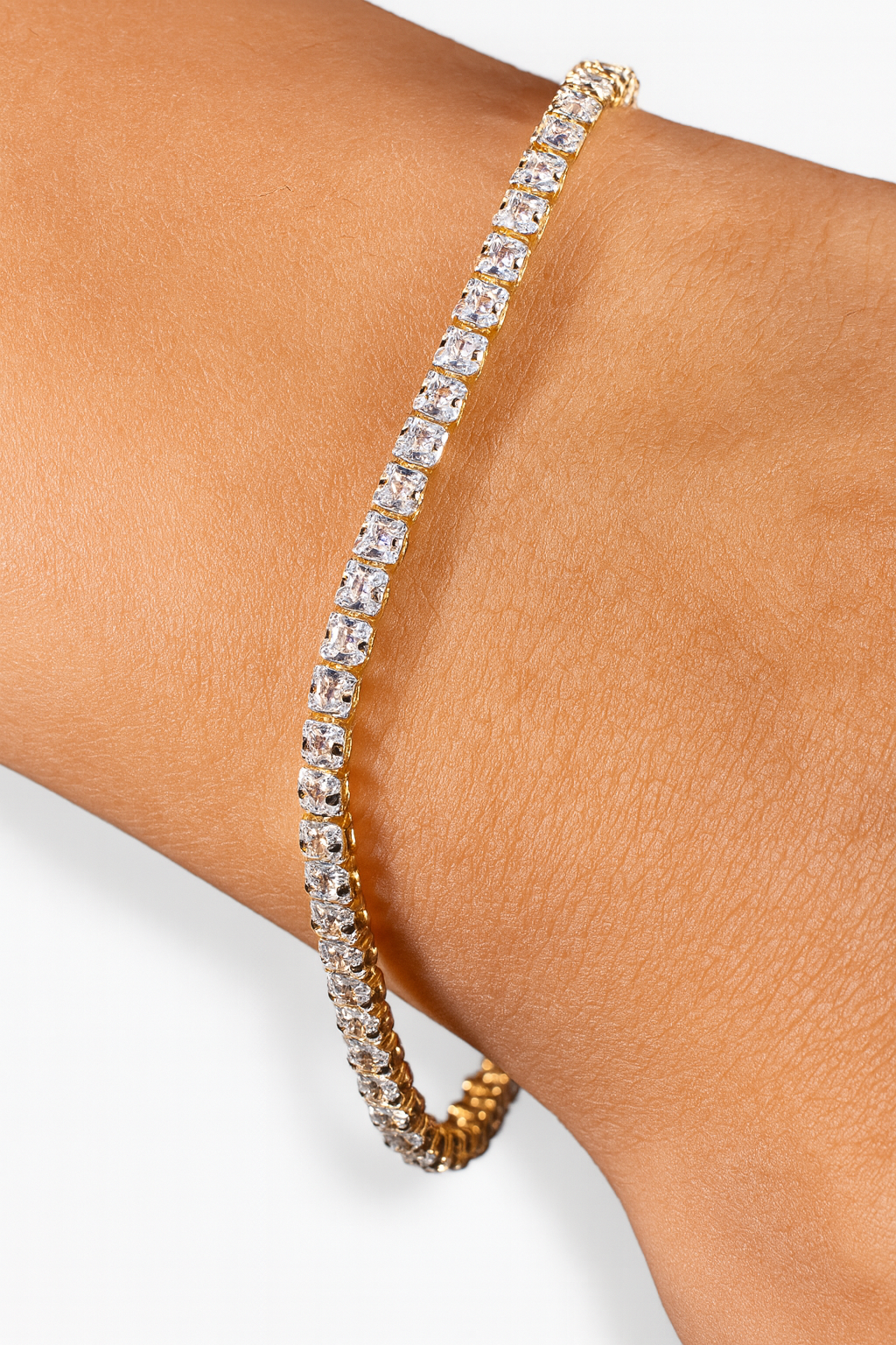 Gold bracelet with clear stones on a wrist against a light background