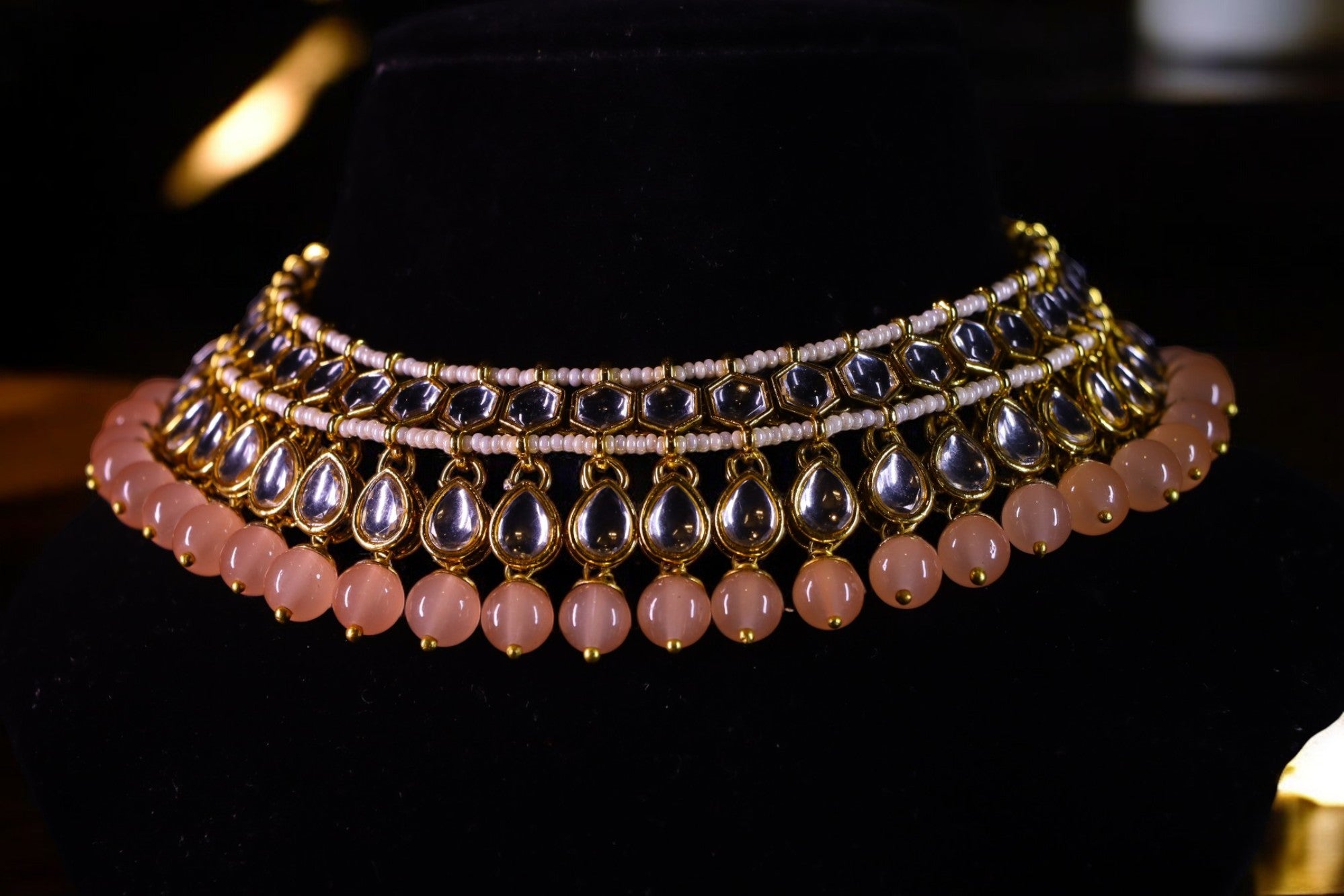 A close-up of a pastel pink and gold-colored kundan necklace set